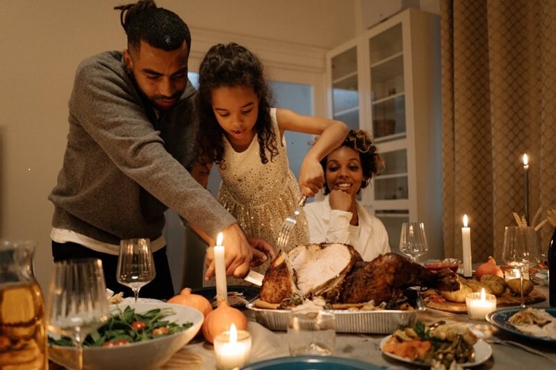 Family enjoying a Thanksgiving dinner. The father is helping the young daughter to slice the turkey while the mother looks on