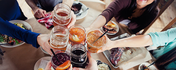 Alcoholic Drink Recipes Group of friends clinking glasses at a table with food.